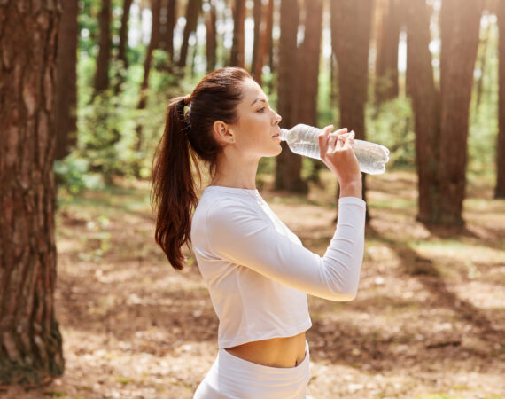 profile portrait beautiful relaxed athlete european woman white sport wear standing resting holding bottle drinking while looking away